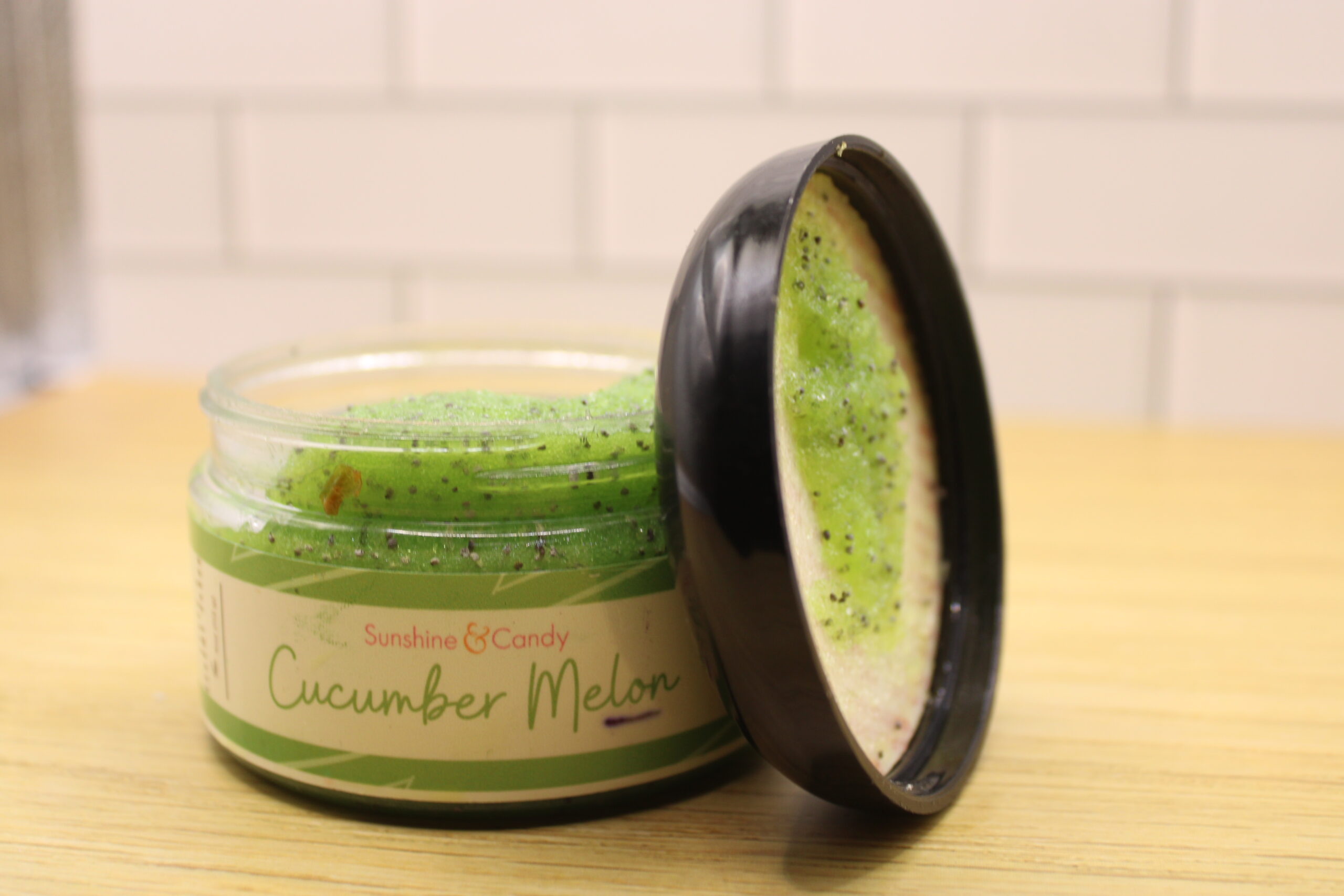 Jar of All-Natural Sugar & Sesame Seed Scrub with visible organic cane sugar and sesame seeds, surrounded by fresh cucumber and melon slices.Jar of All-Natural Sugar & Sesame Seed Scrub with visible organic cane sugar and sesame seeds, surrounded by fresh cucumber and melon slices.